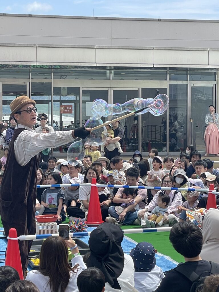 シャボン玉おじさんがとばした大きなシャボン玉に、最前列の子どもたちが手をのばしている
