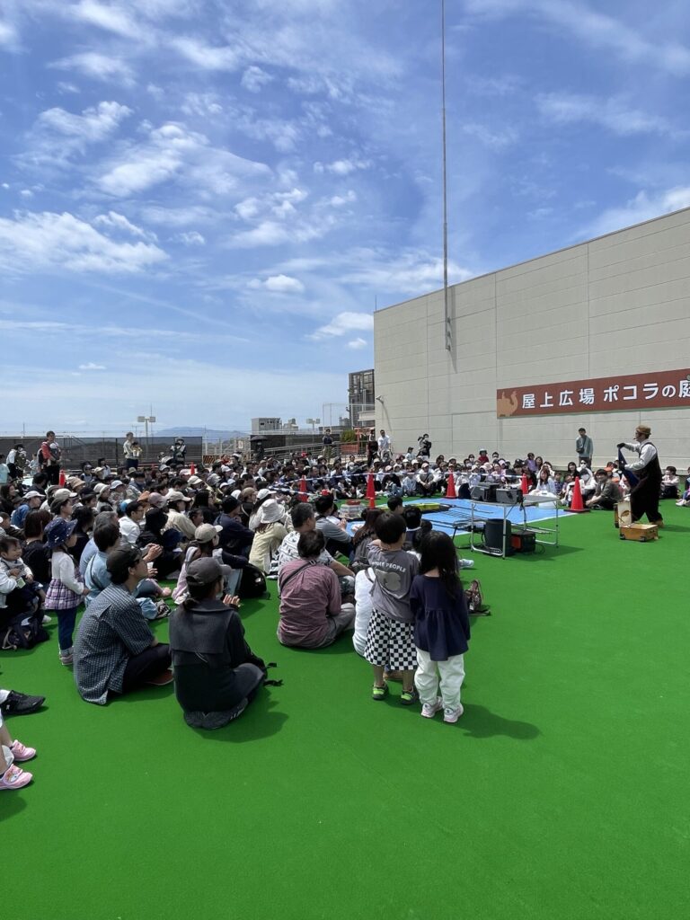 ならファミリー屋上広場「ポコラの庭」の人工芝の会場でシャボン玉ショーを見る親子連れ