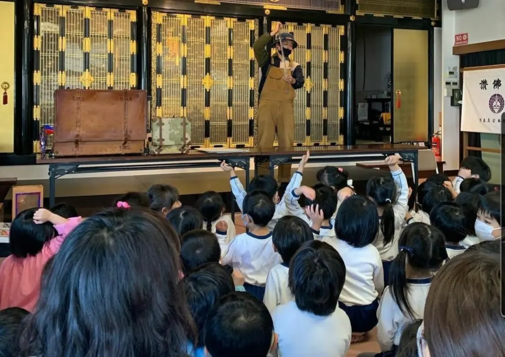 園の講堂のステージでシャボン玉をとばすシャボン玉おじさんと、手をのばす園児たち