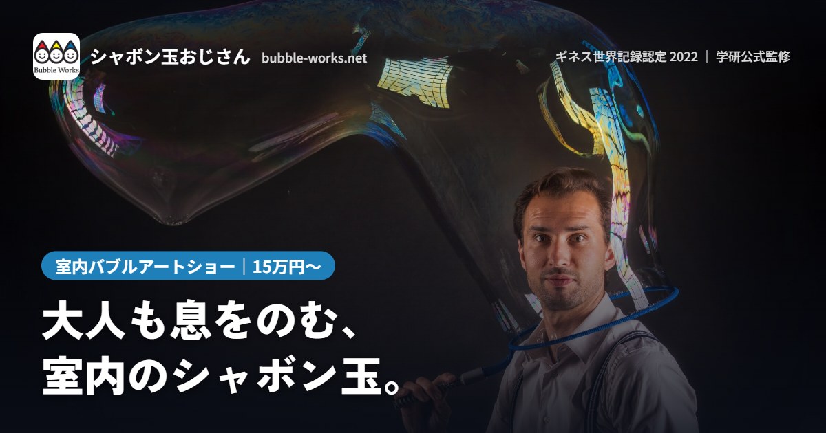 暗い舞台で巨大なシャボン玉をつくるシャボン玉おじさん。室内バブルアートショー